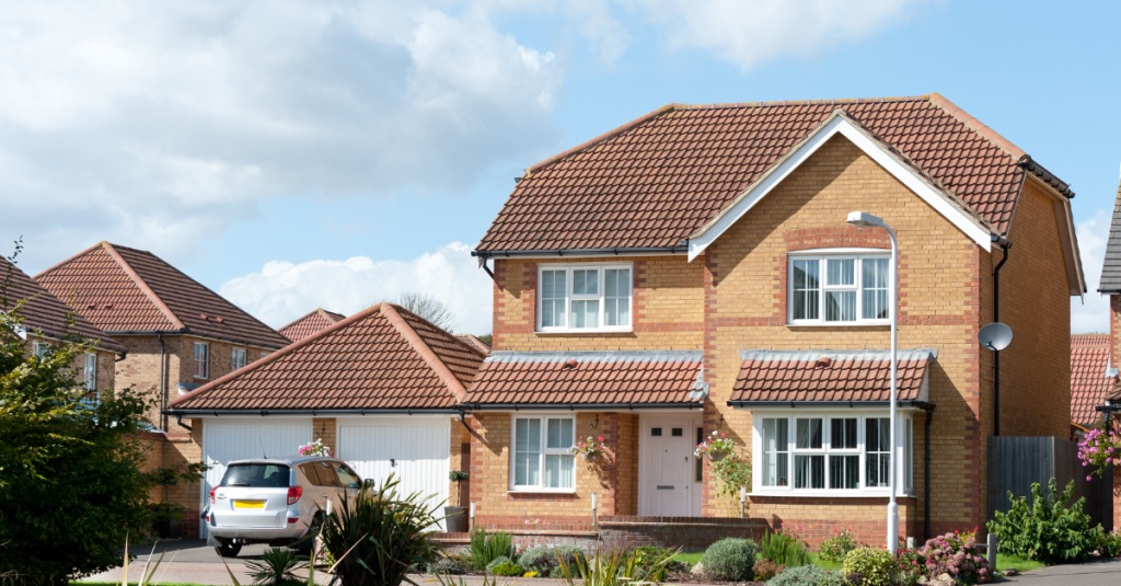 Driveway view of a brick home and detached garage with a car parked in front
