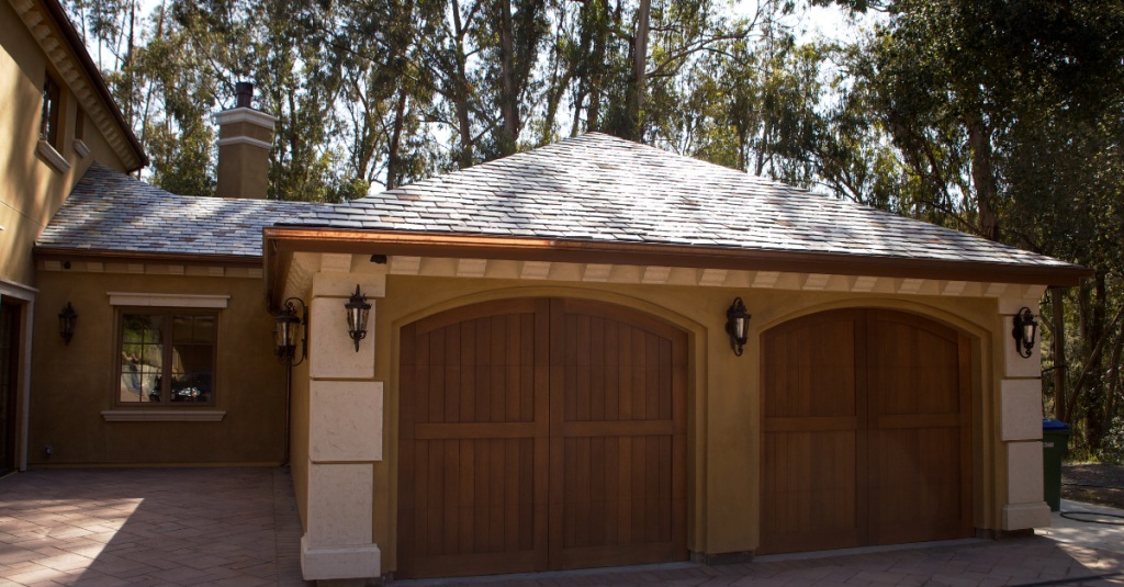 Attached garage with arched wooden doors and brick columns