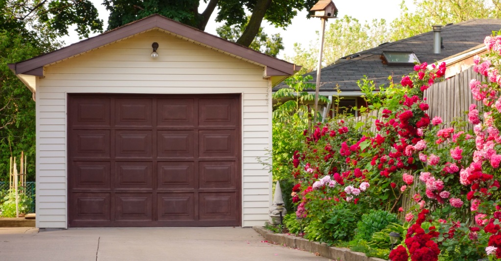 Detached single-car garage with wood siding and blooming red flowers nearby