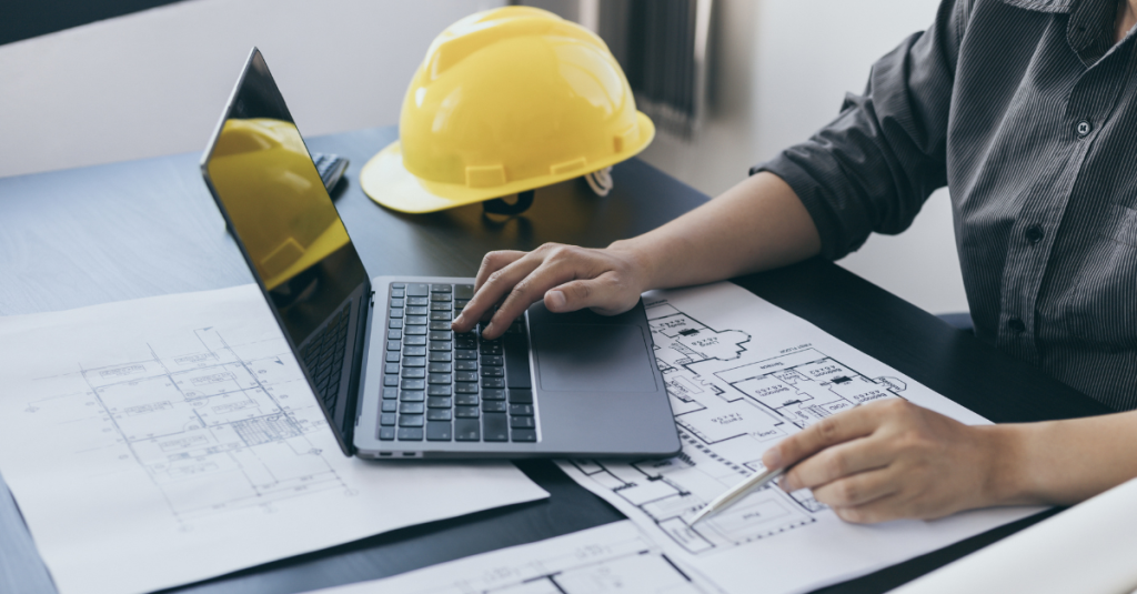 CAPS professional reviewing home plans on laptop with blueprint and hard hat