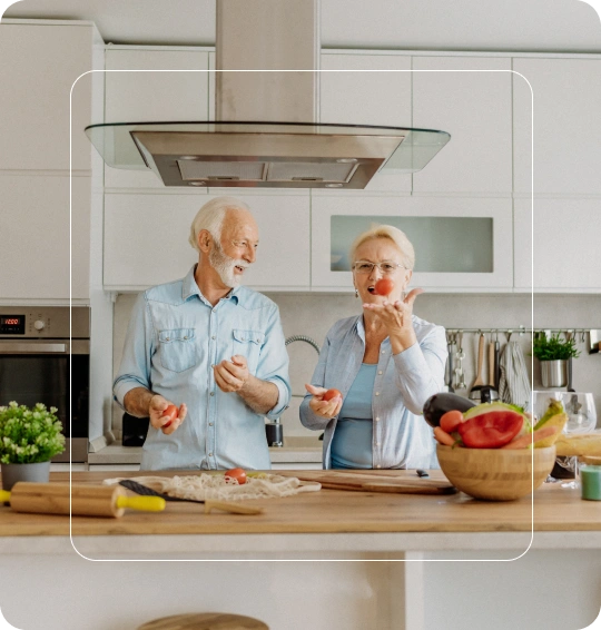 Older couple slicing tomatoes on a wooden kitchen island with white cabinets