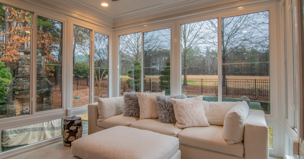 White sectional sofa with textured pillows and a matching ottoman, in a windowed sunroom.