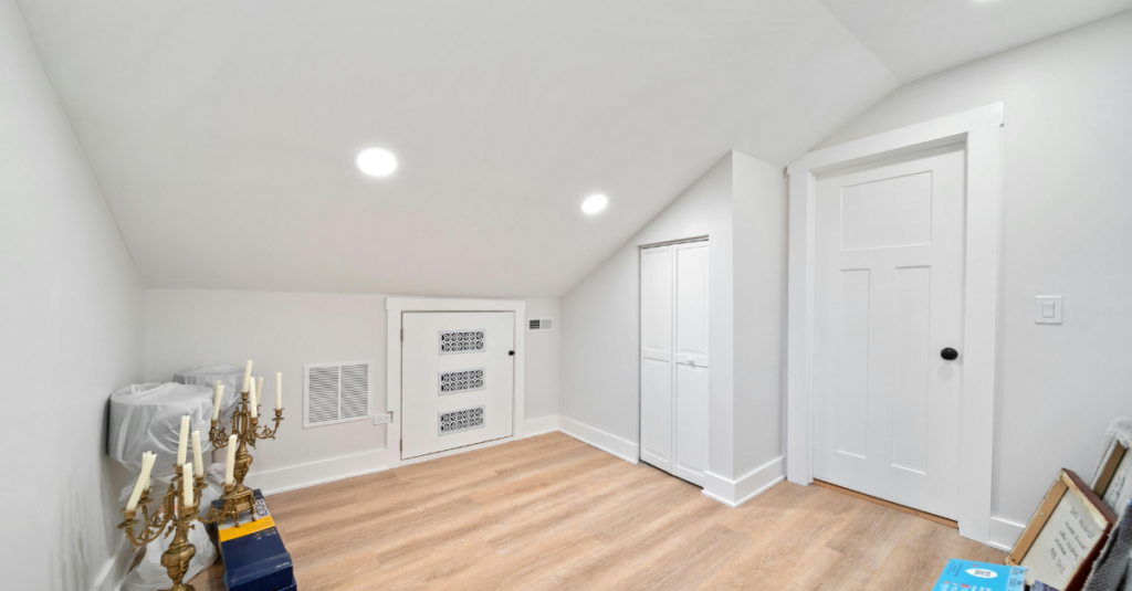 Sloped ceiling attic room with recessed lights, light wood floor, white closet doors.