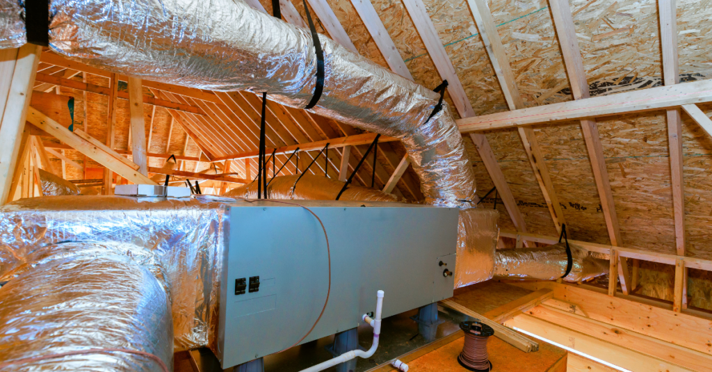 Attic with foil-faced HVAC ducts around a gray air handler and exposed wood framing.