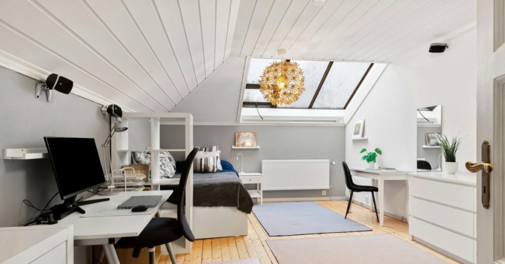 Bright attic with white paneled ceiling, skylight, study desk, bed, and dresser.